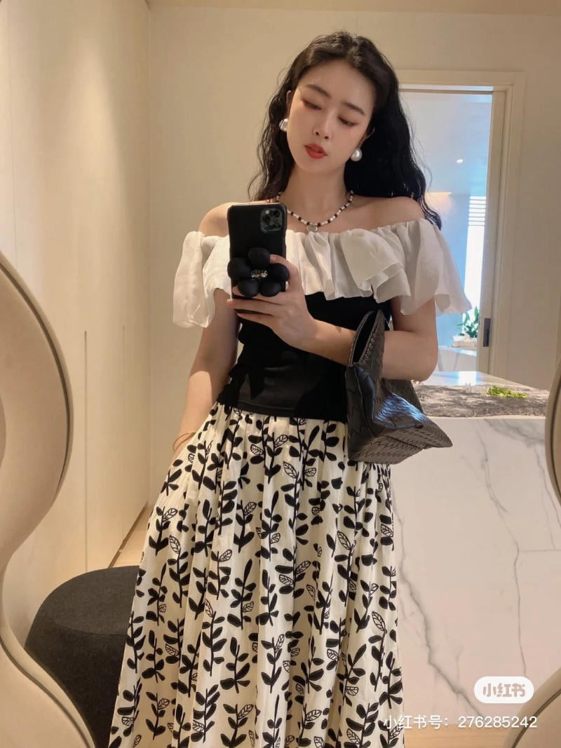 Cô gái mặc áo trễ vai croptop trắng họa tiết và chân váy hoa nhí, đeo khuyên tai ngọc trai