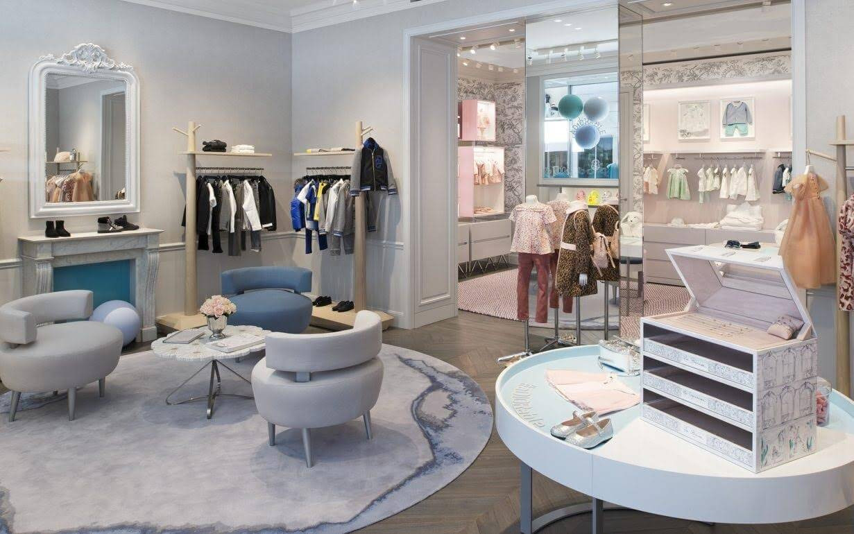 Cách bày trí sản phẩm trong mẫu shop quần áo trẻ em sơ sinh với bàn trưng bày thấp và đồ trang trí đáng yêu